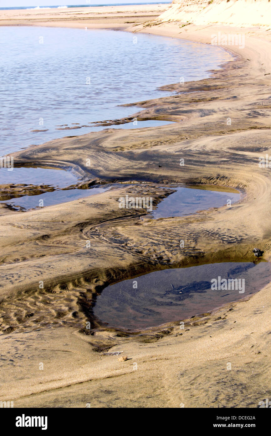 A lagoon inlet to the ocean at low tide showing the waterline surrounded by sand dunes Stock Photo