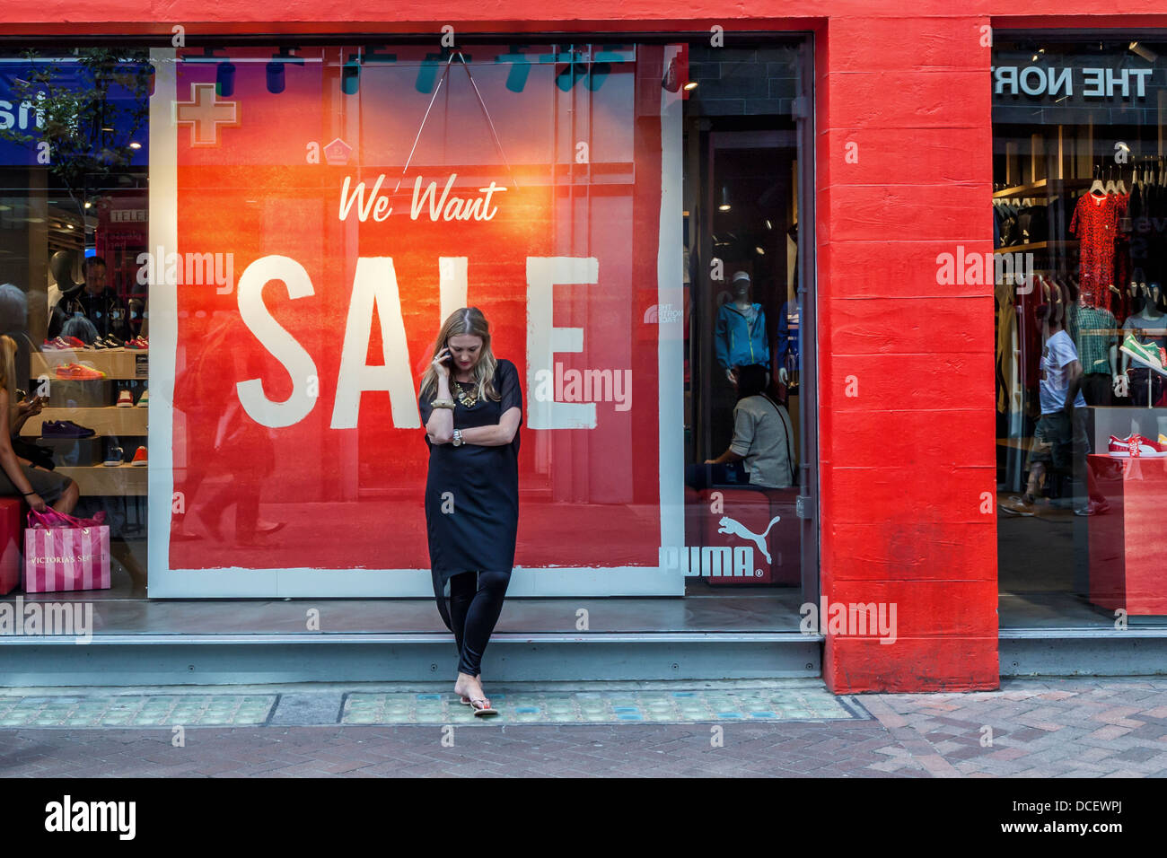Woman using mobile phone in front of Puma Store with red "We want Sale"  sign in window - Carnaby Street, London Stock Photo - Alamy