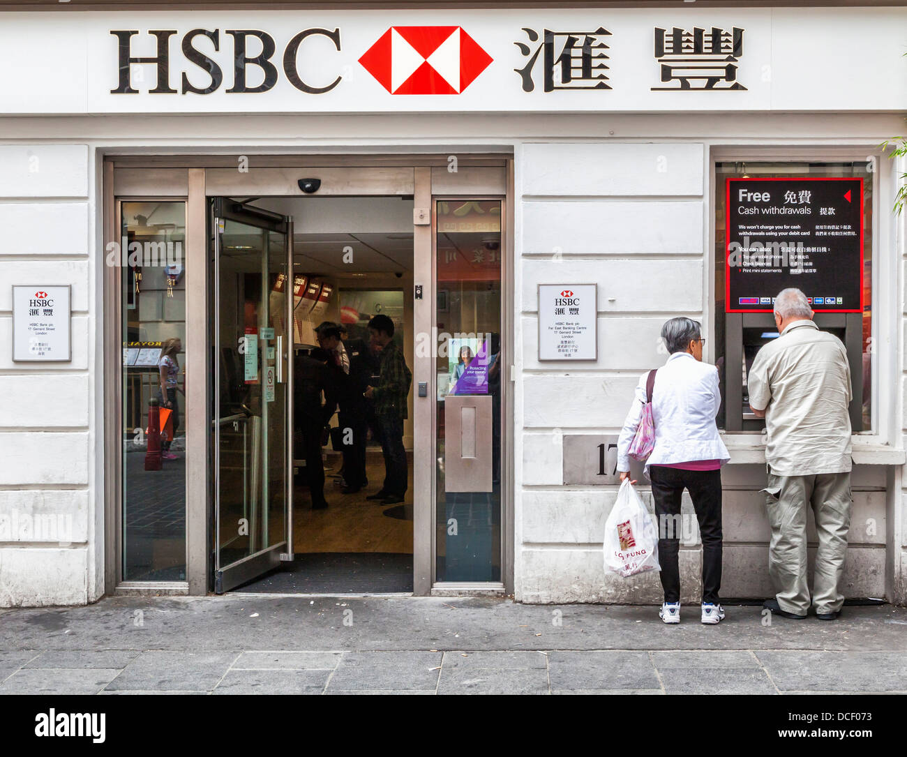 Senior man and woman use ATM under bilingual lettering of the HSBC bank, Gerrard Street, ChinaTown, London W1 Stock Photo