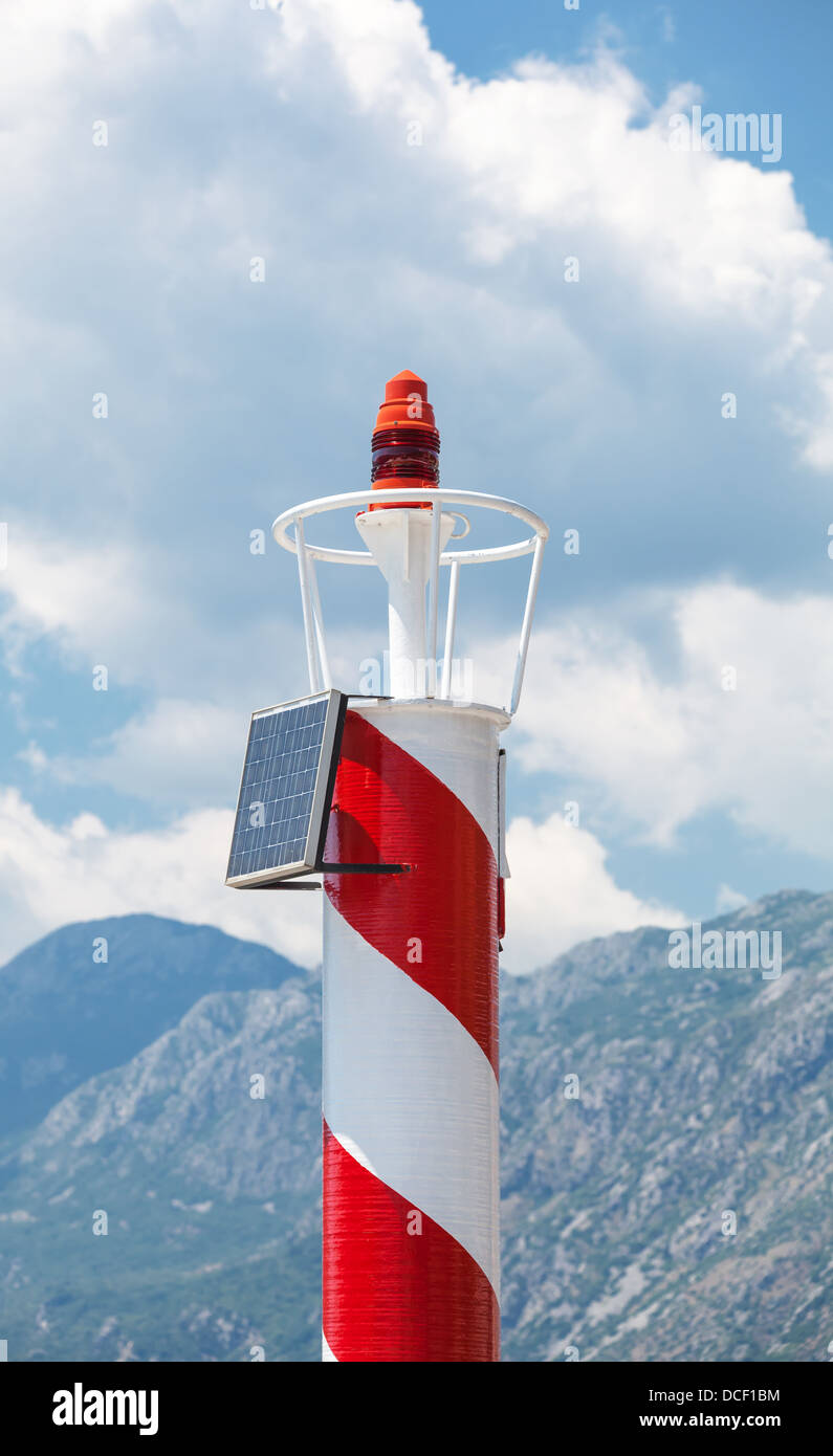 Rad and white striped lighthouse above cloudy sky. Central pier of Perast town, Montenegro Stock Photo