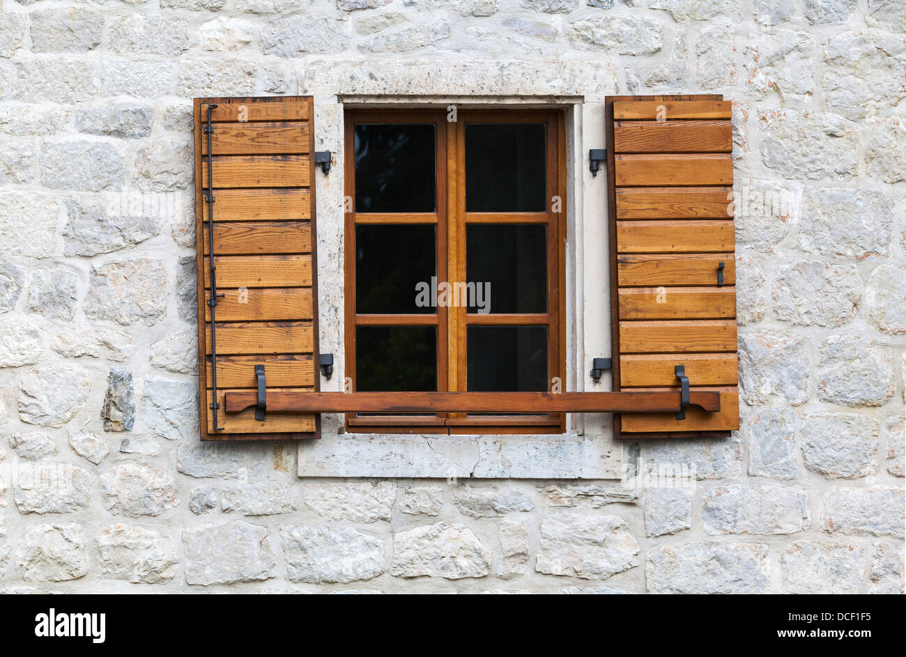 Wooden window with open jalousies in old gray stone wall Stock Photo
