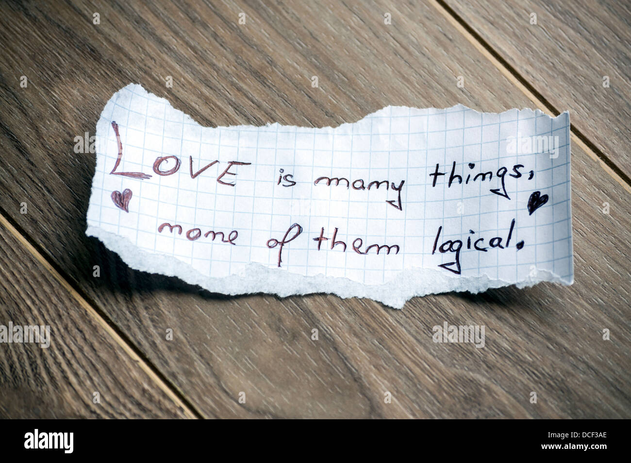 Love is many things, none of them logical (Quote by William Goldman) - Hand writing text on a piece of paper on wood background Stock Photo