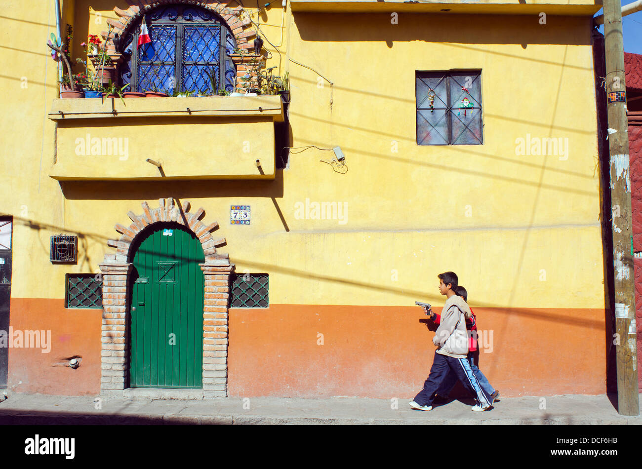 Two boys walking on sidewalk carrying gun; San Miguel de Allende, Guanajuato, Mexico Stock Photo