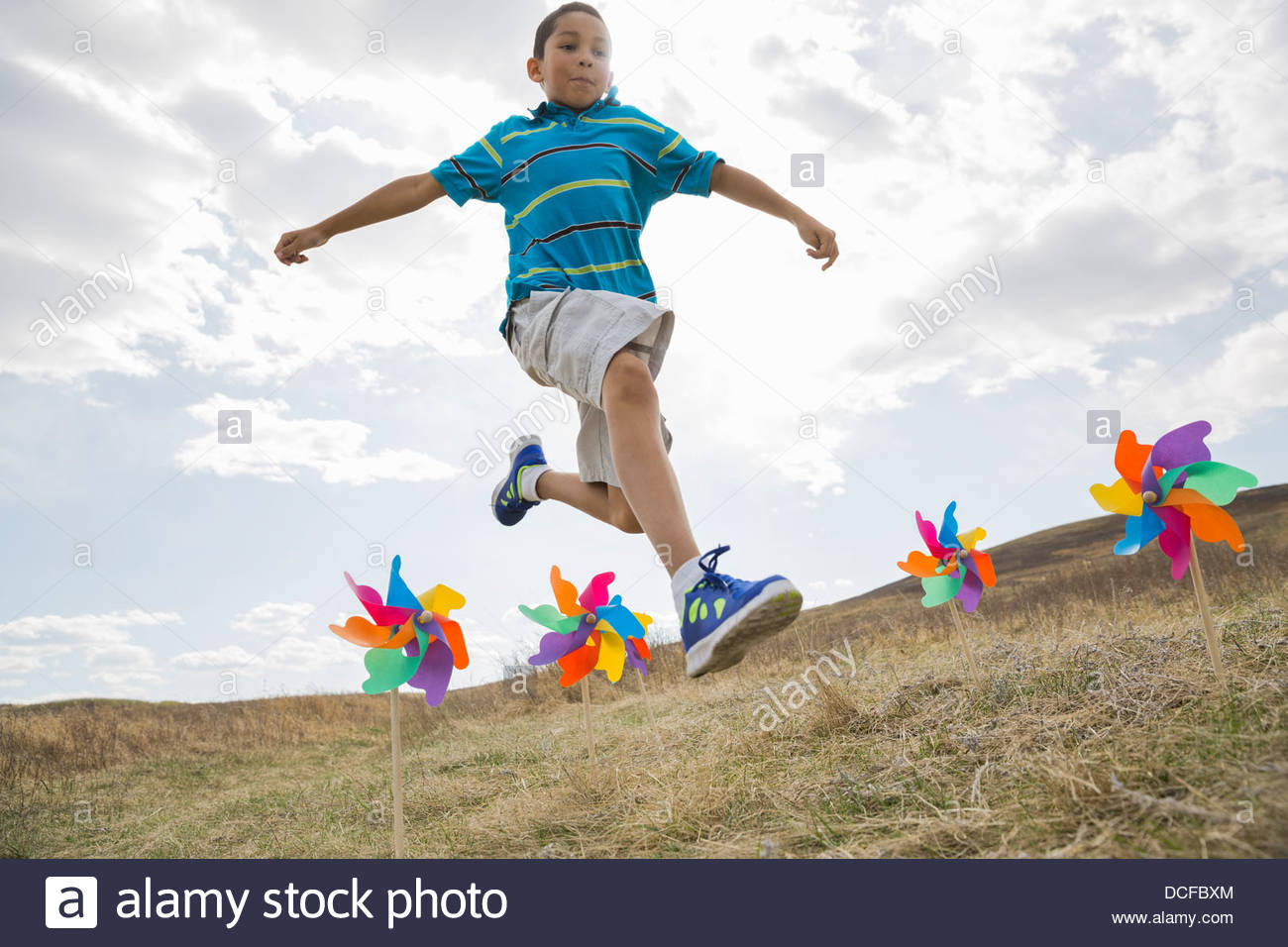 Schoolboy jumping over pinwheels in field Stock Photo