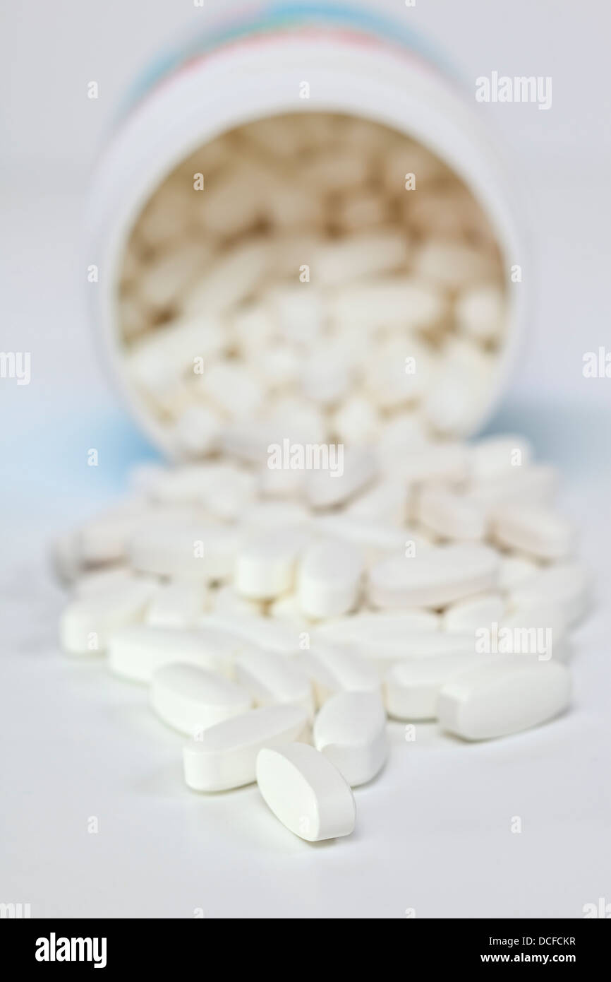Pills Spilling from Container - white vitamin pills spilling from container, shallow DOF, focus on foreground. Stock Photo