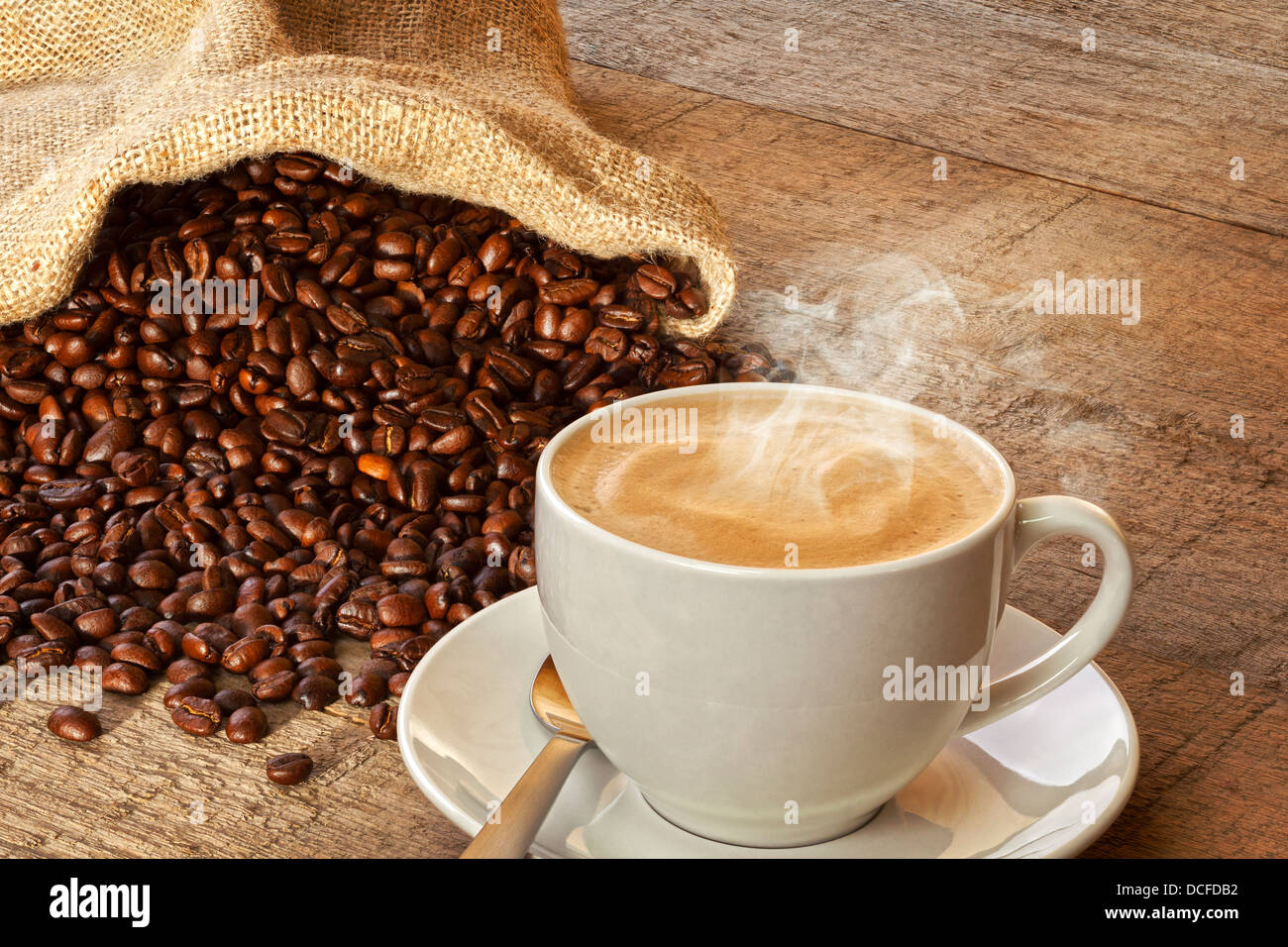 Coffee and Sack of Coffee Beans - a cup of hot steaming espresso coffee on a rustic plank background, with a sack of coffee... Stock Photo