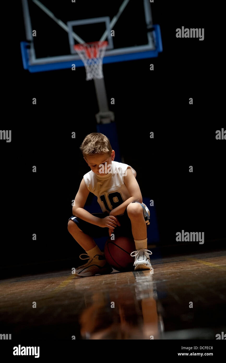 Young Boy Sitting On Basketball Court Looking Solemn Stock Photo