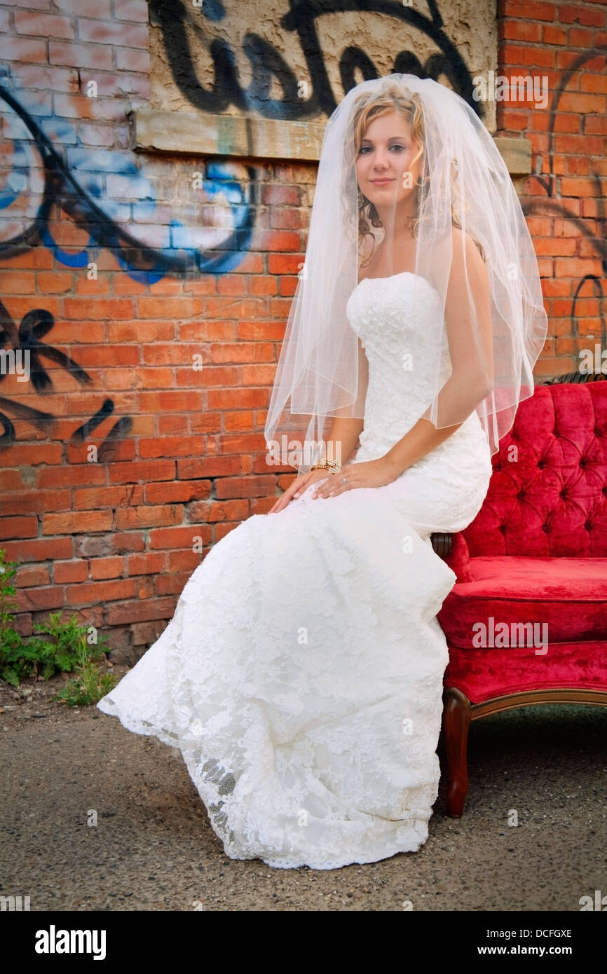 Bride Sitting On The Edge Of A Red Sofa Outdoors Stock Photo