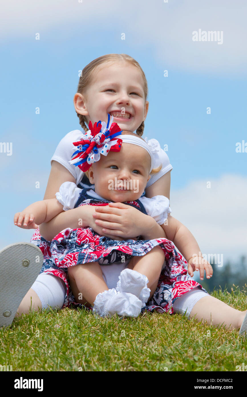 A Girl Holding Her Baby Sister On The Grass; Portland, Oregon, United States Of America Stock Photo