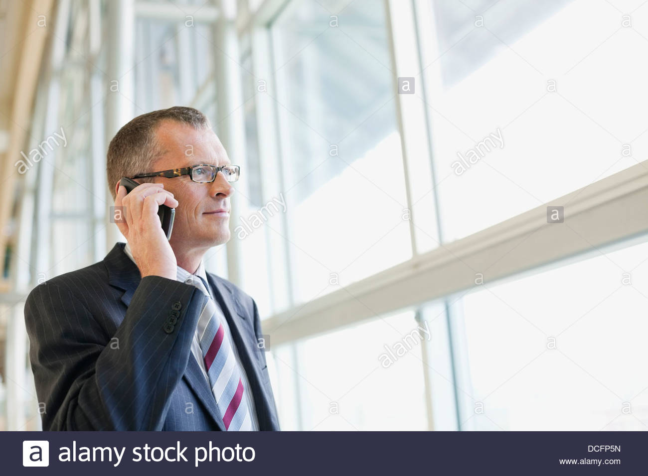 Businessman talking on mobile phone by window Stock Photo