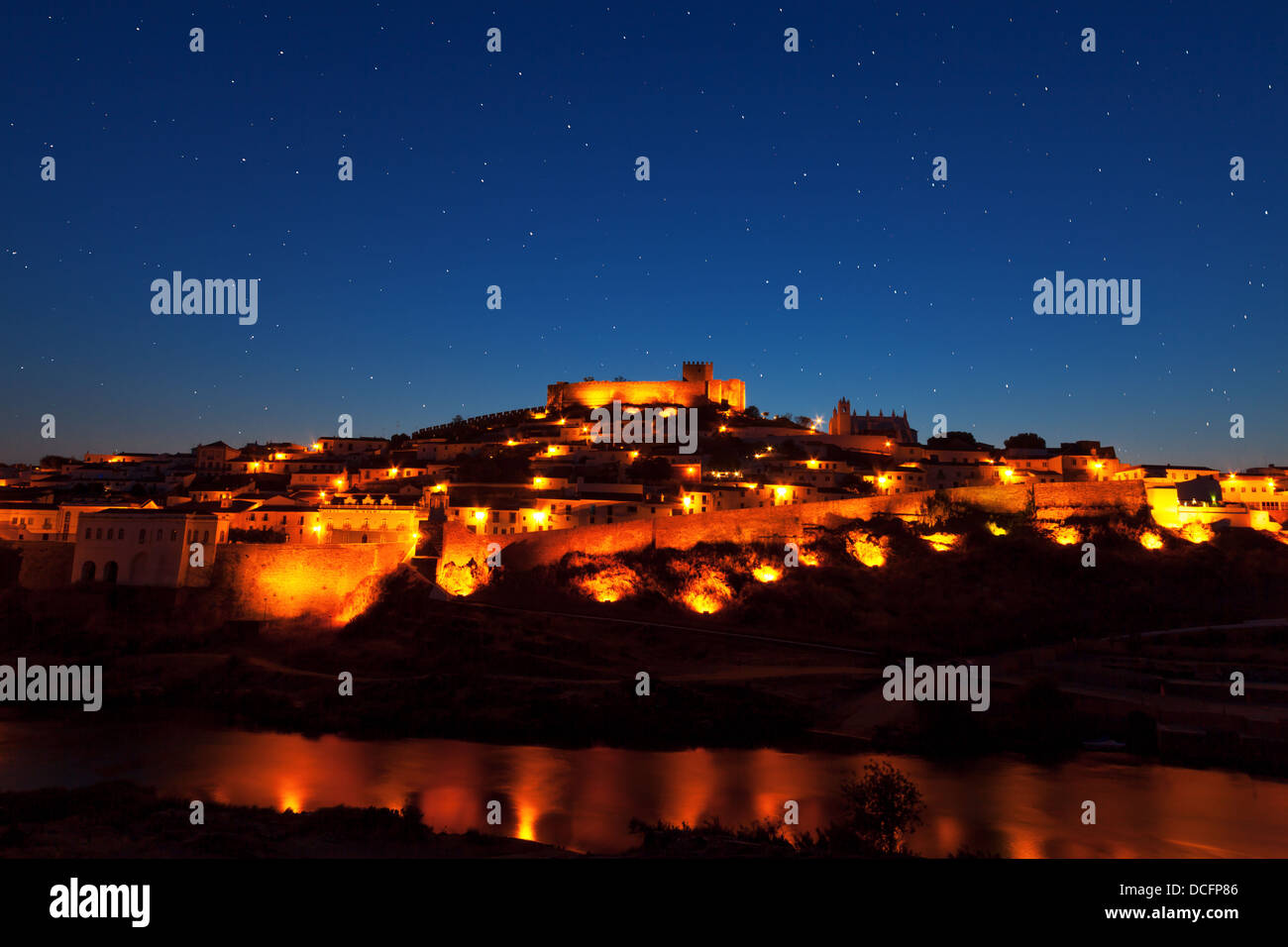 Walled town illuminated at night reflected in still water with a fortified castle on the brow of the hill overlooking the town Stock Photo