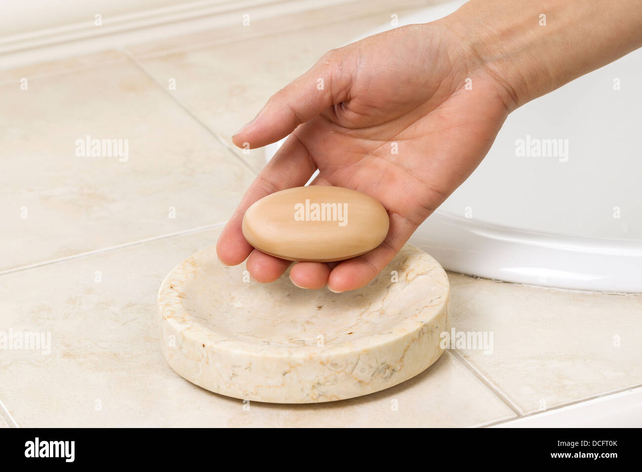 Horizontal photo of female hand holding bar of soap with bathroom sink