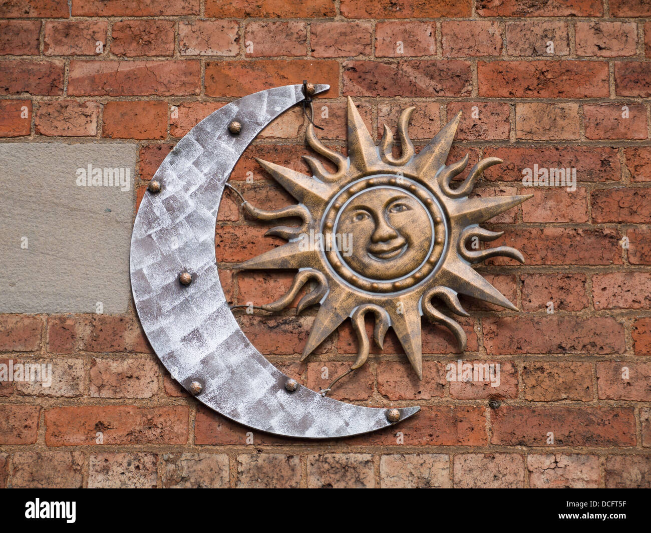 Copper sign of a moon and smiling sun hanging on a red brick wall. Stock Photo