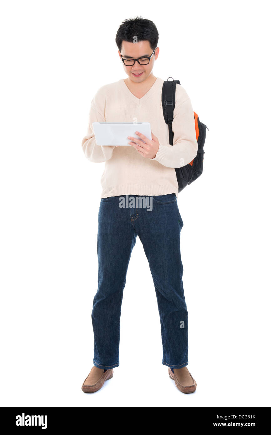 Full body Asian adult student in casual wear with school bag using digital computer tablet pc standing isolated on white background. Asian male model. Stock Photo