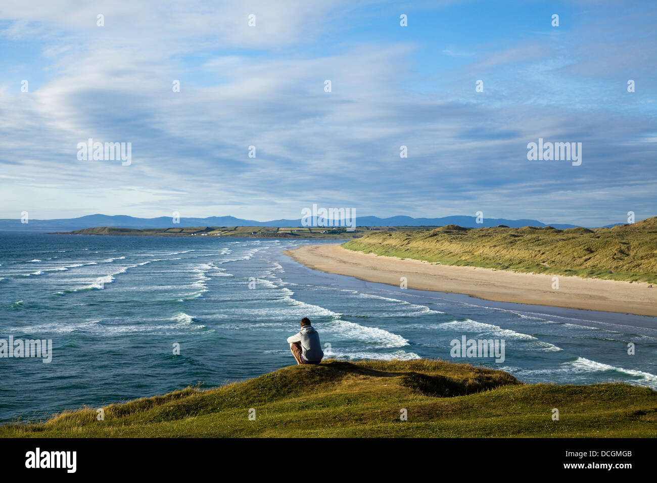 A Person Sitting At The Water's Edge At The Beach Near Bundora; County Donegal, Ireland Stock Photo