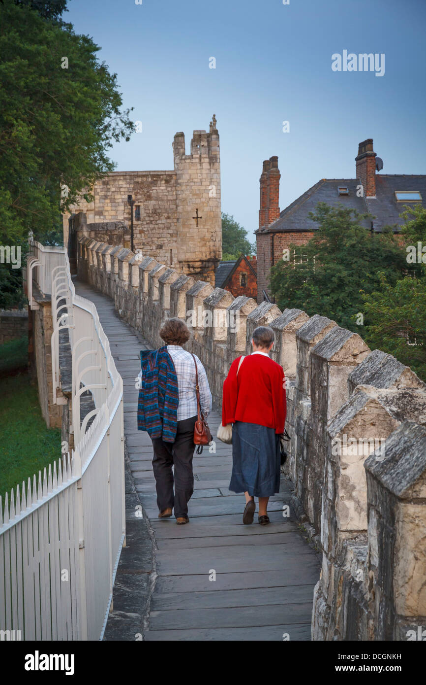 Two 2 people walking on walled York City bar roman wall walls towards Micklegate old ceremonial entrance Yorkshire, England. Stock Photo