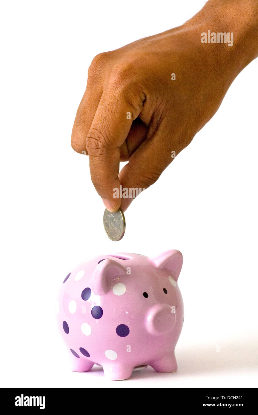 A hand placing a coin into a cute piggy bank Stock Photo - Alamy