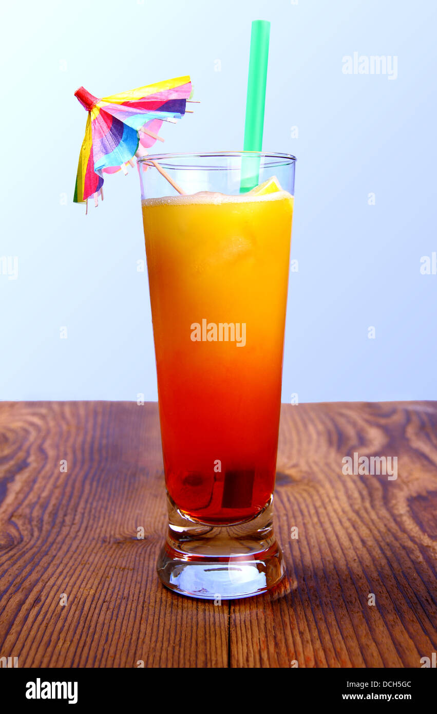 Red, yellow cocktail with lemon, straw with umbrella deco, vertical Stock Photo