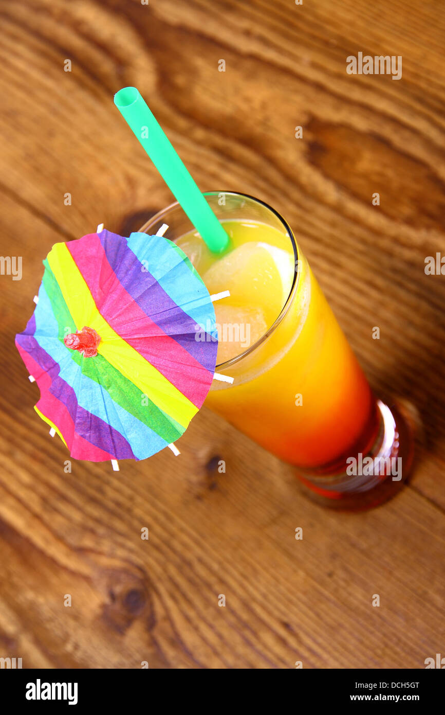 Red, yellow cocktail with lemon, straw and umbrella deco, top view Stock Photo