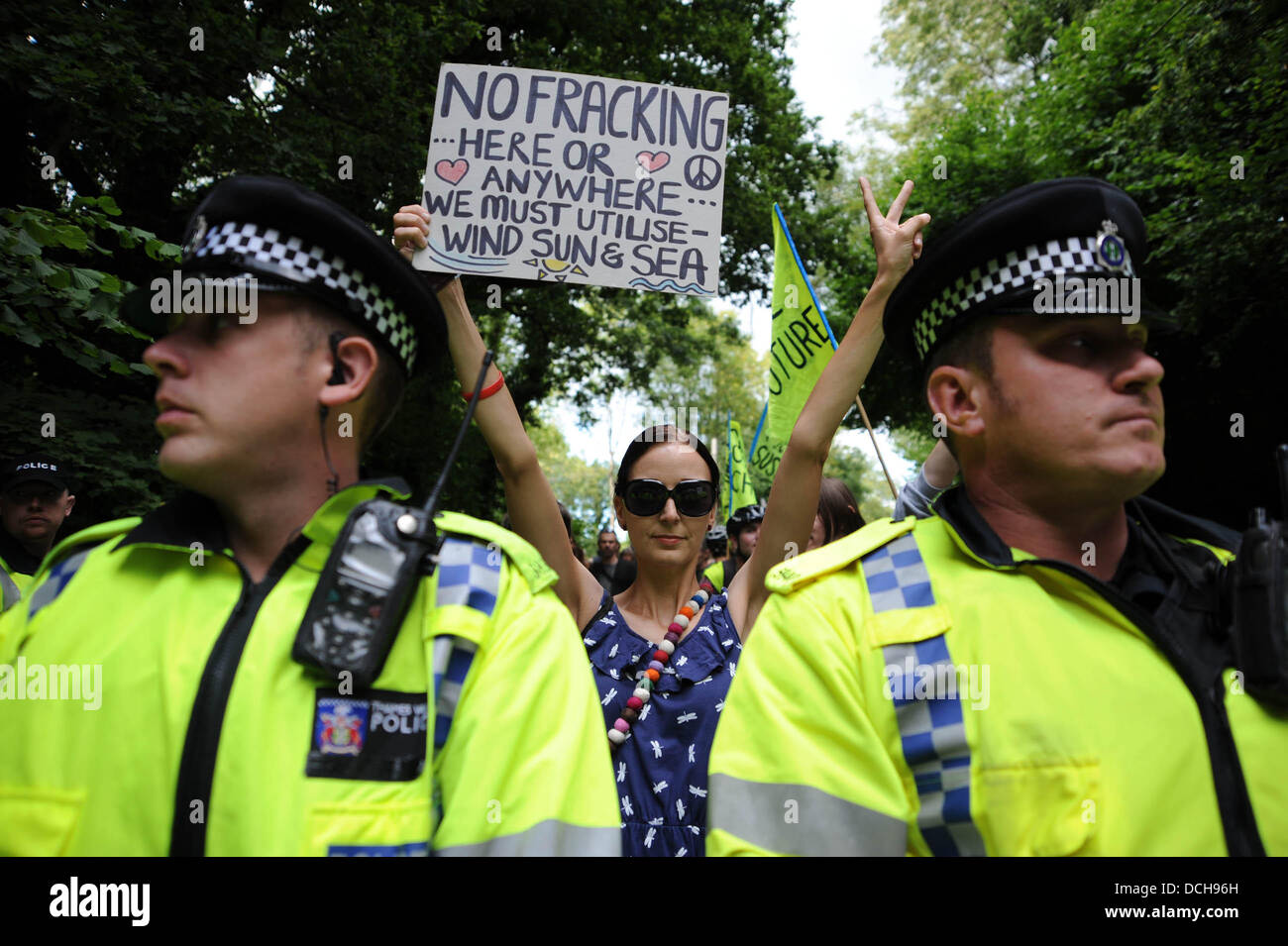 Balcombe, West Sussex, UK. 18th August 2013. A young woman holds up a poster behind police line as thousands of protesters converged on Balcombe in West Sussex today to march and protest against the Cuadrilla fracking site in the village . Photograph taken by Simon Dack/Alamy Live News Stock Photo