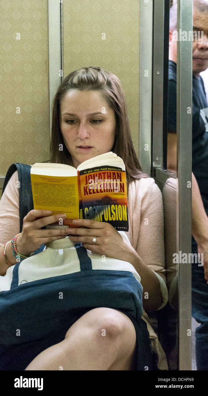 pretty young woman sitting on board subway R train quietly absorbed in reading bestselling mystery novel New York City Stock Photo