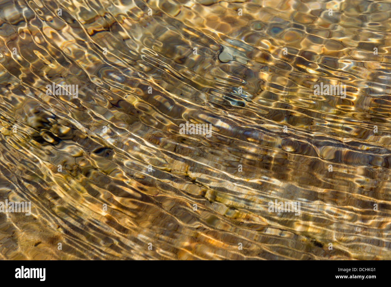 Colourful golden abstract circular water ripples above sunlit rocky stream bed, UK Stock Photo