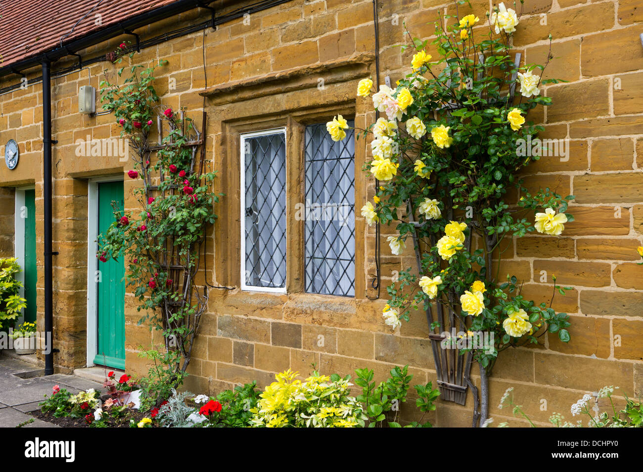 Terrace of old stone cottages with flower borders and roses growing around one window. Stock Photo