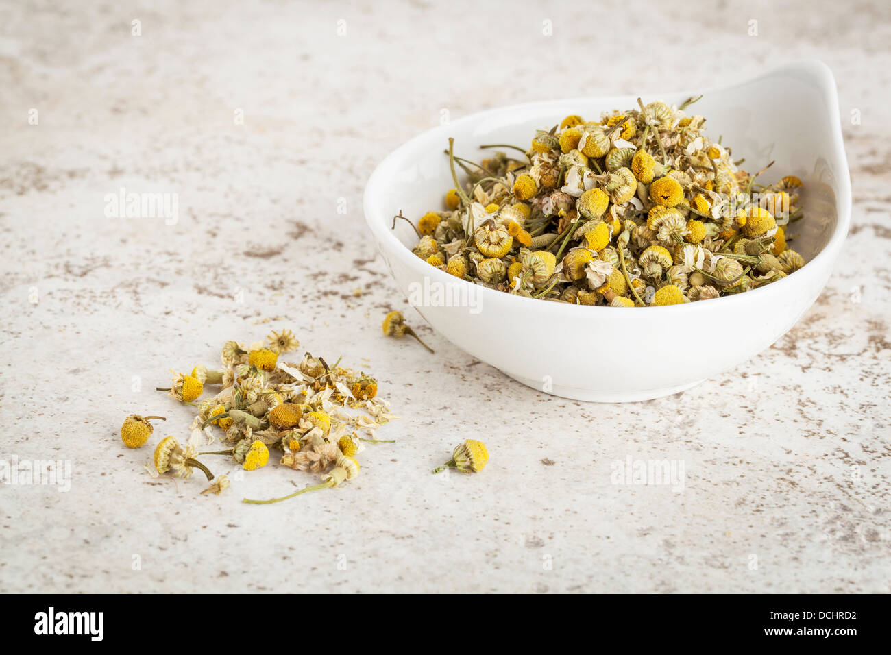 small ceramic bowl of dried chamomile flowers against a ceramic tile background Stock Photo
