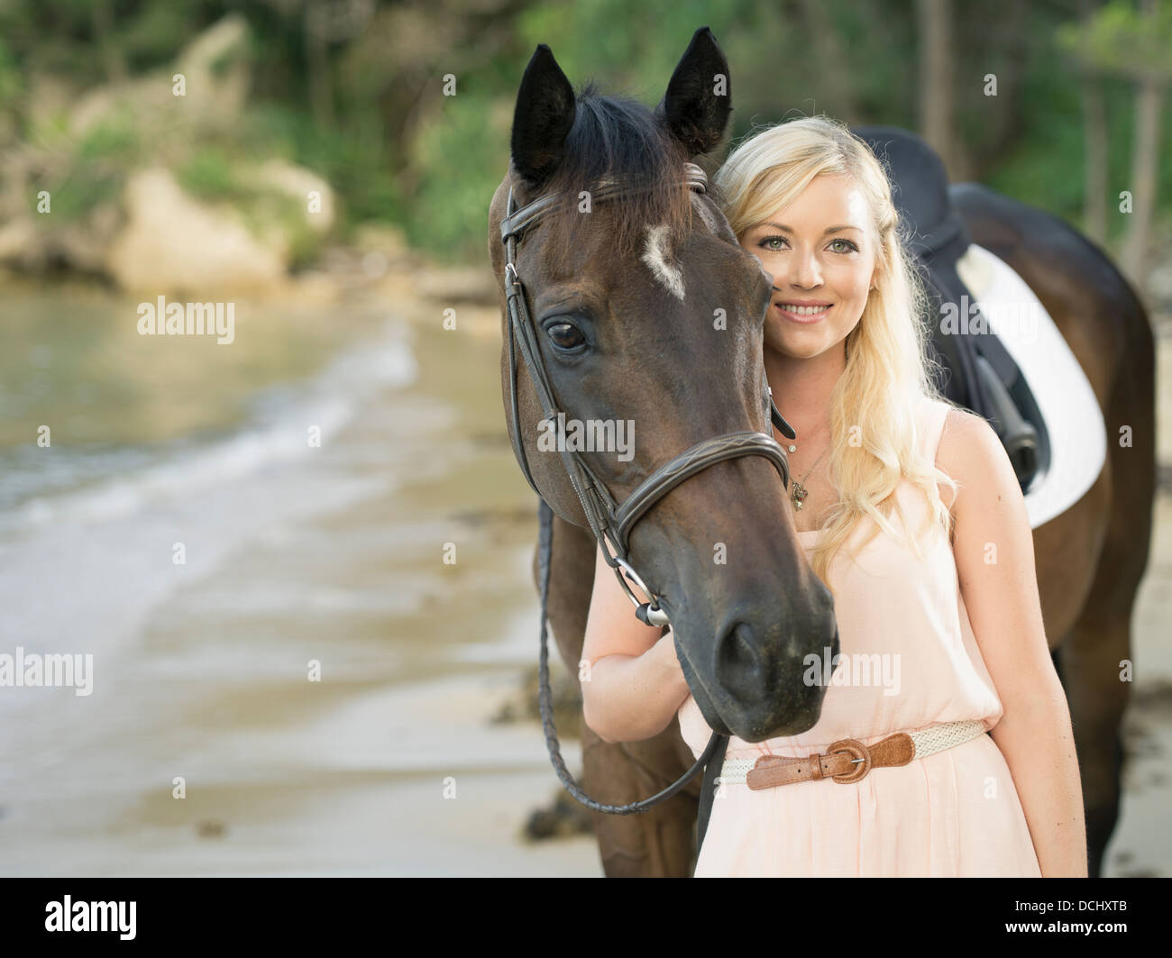 Beautiful  blonde Caucasian woman with dark brown thoroughbred / gelding horse on the beach Stock Photo