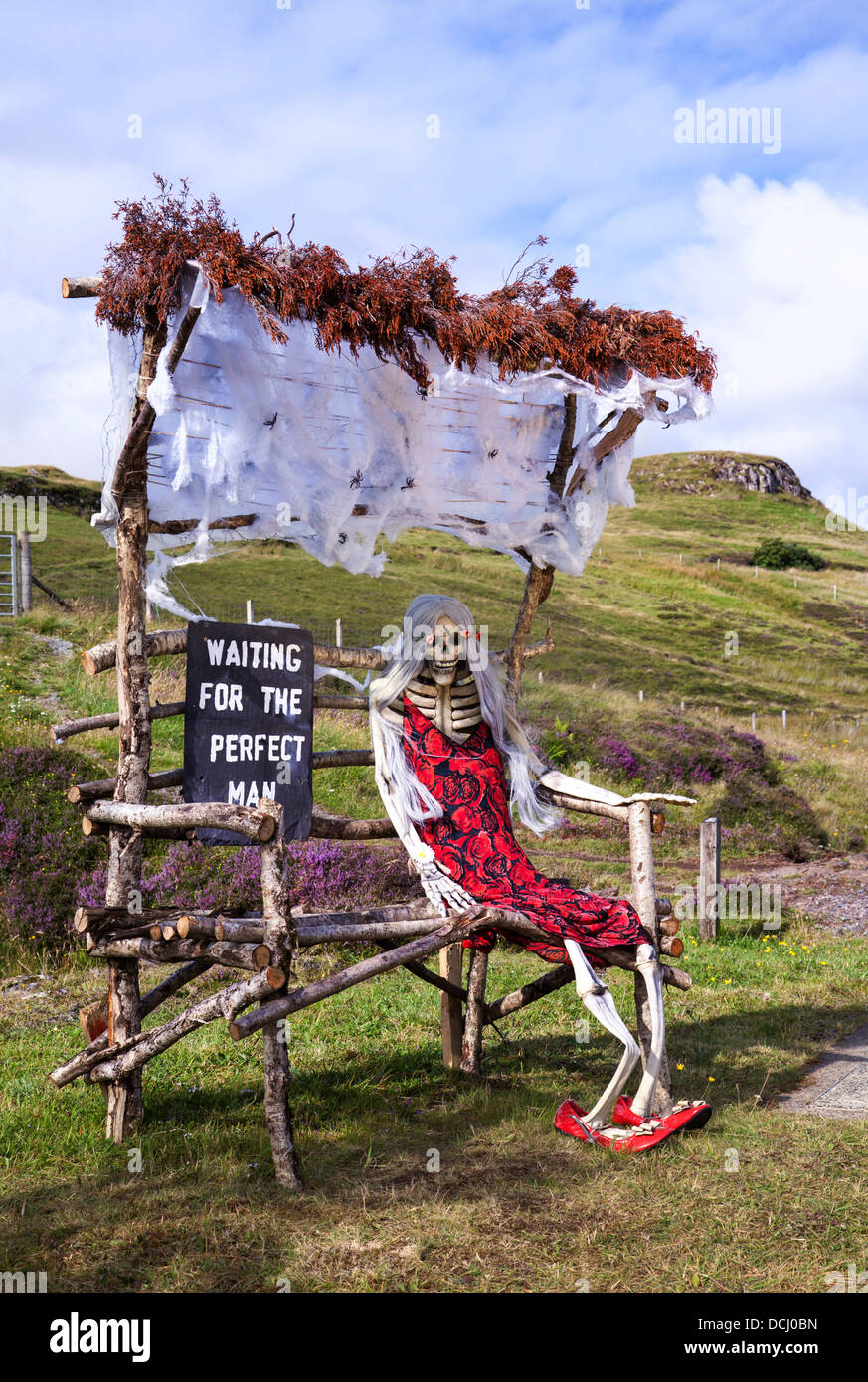 Waiting for the perfect man, Lonely Scary Skeleton in a red dress, sat on ricktey upcycled recycled wooden bench. Carbost, Isle of Skye, Scotland, UK Stock Photo