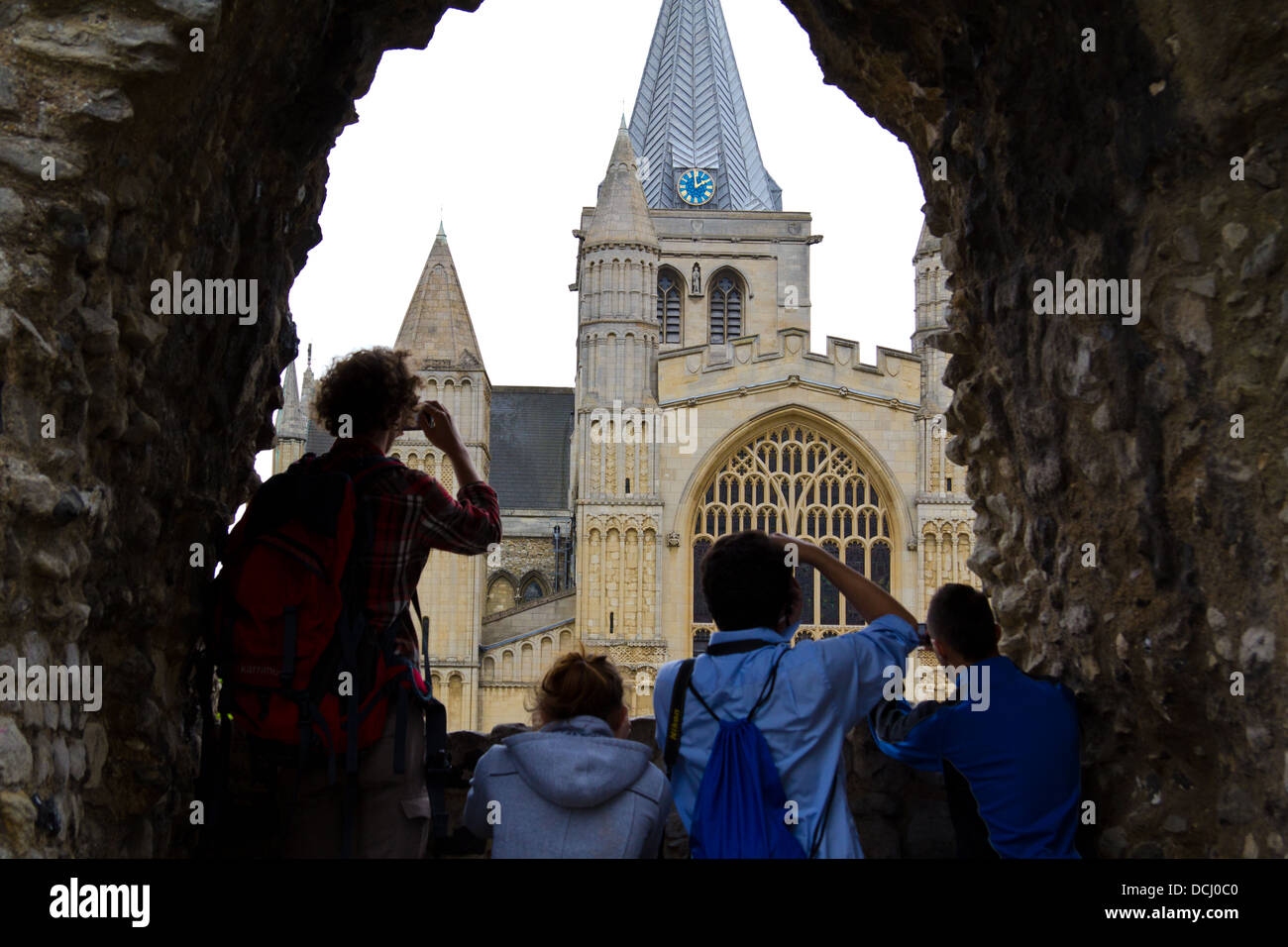 Image of  visitors photographing Rochester Cathedral through a window made in a stone wall on a grey summer day Stock Photo