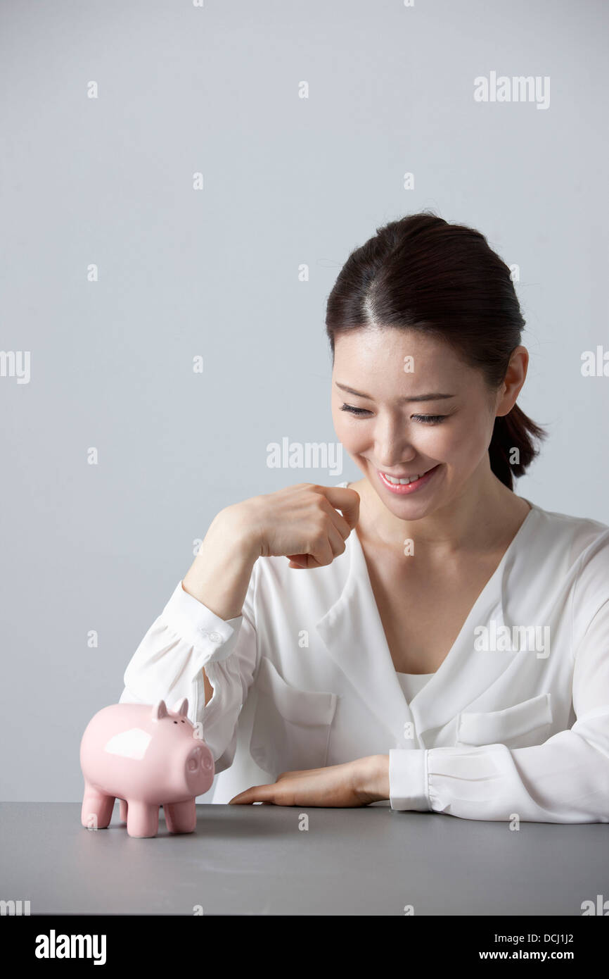 a woman smiling at desk with a piggy bank Stock Photo - Alamy