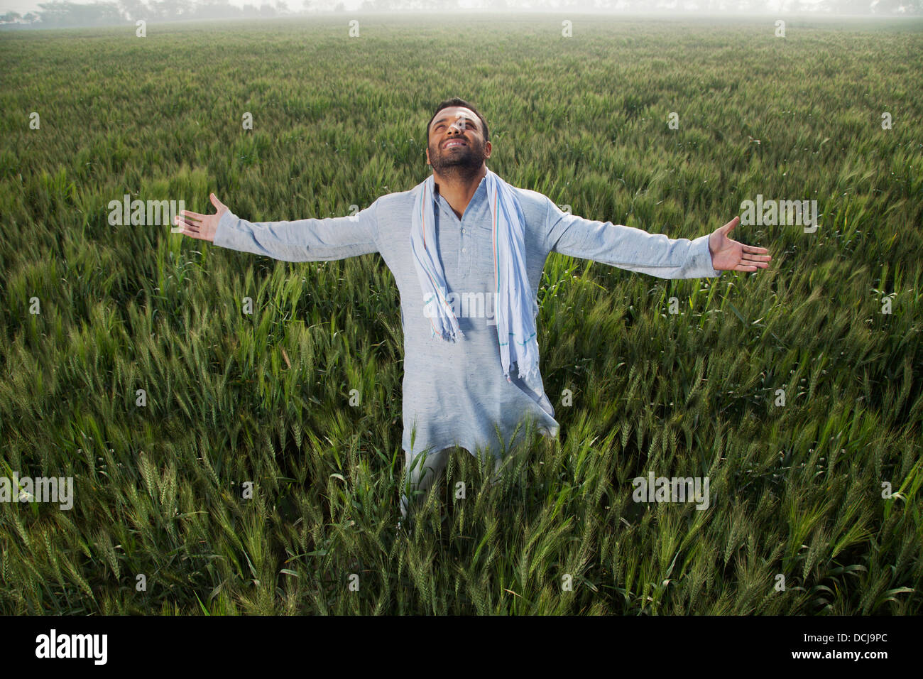 Indian man standing in field with arms out Stock Photo
