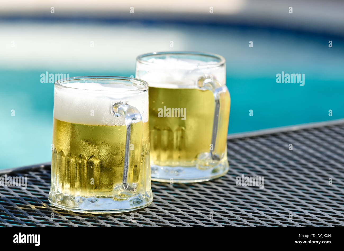 Two cold beer glasses on the table by blue swimming pool on a sunny