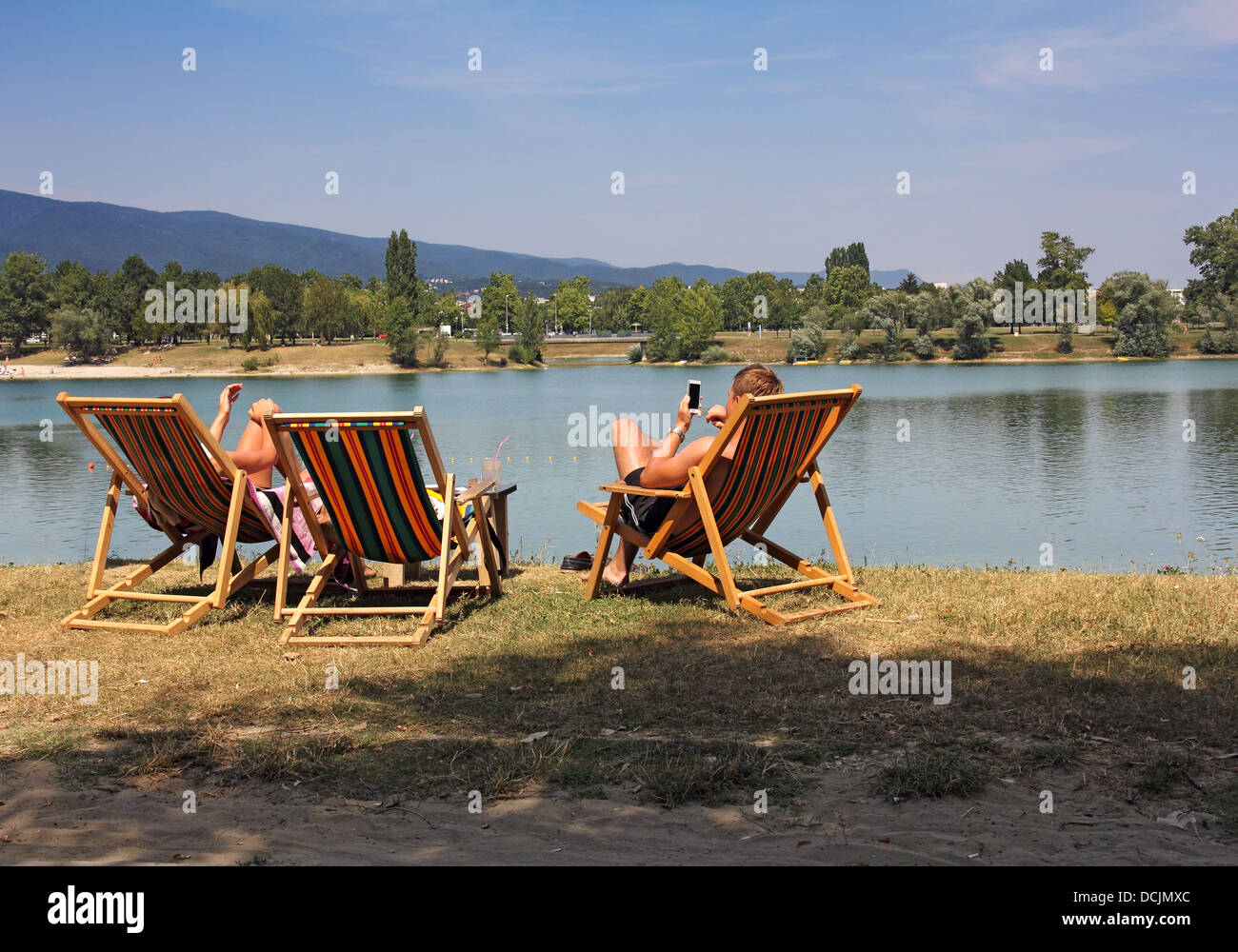 Two young people in colorful deckchairs on the lake shore Stock Photo ...