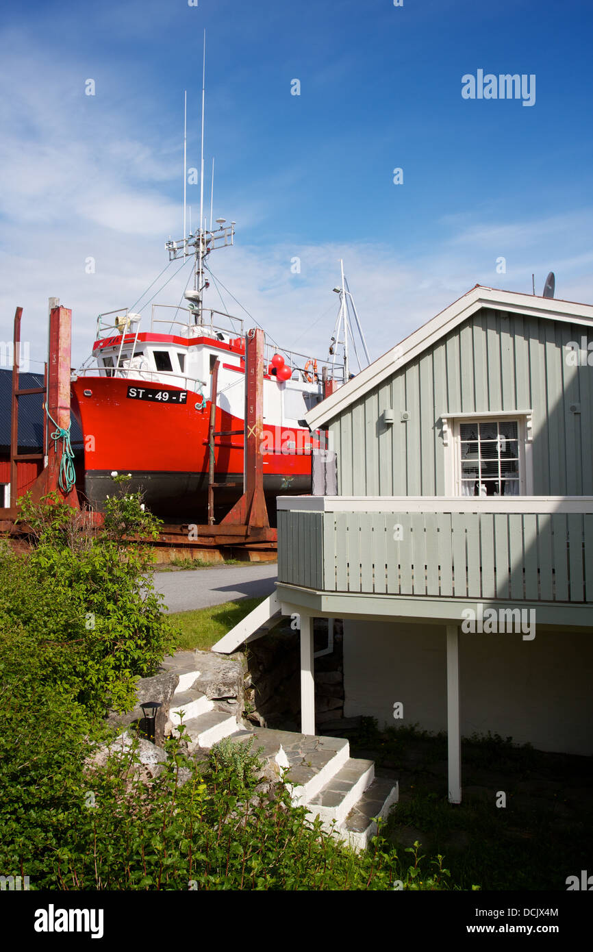 Bright red Norwegian fishing boat in dry dock next to clapboard house. Stock Photo