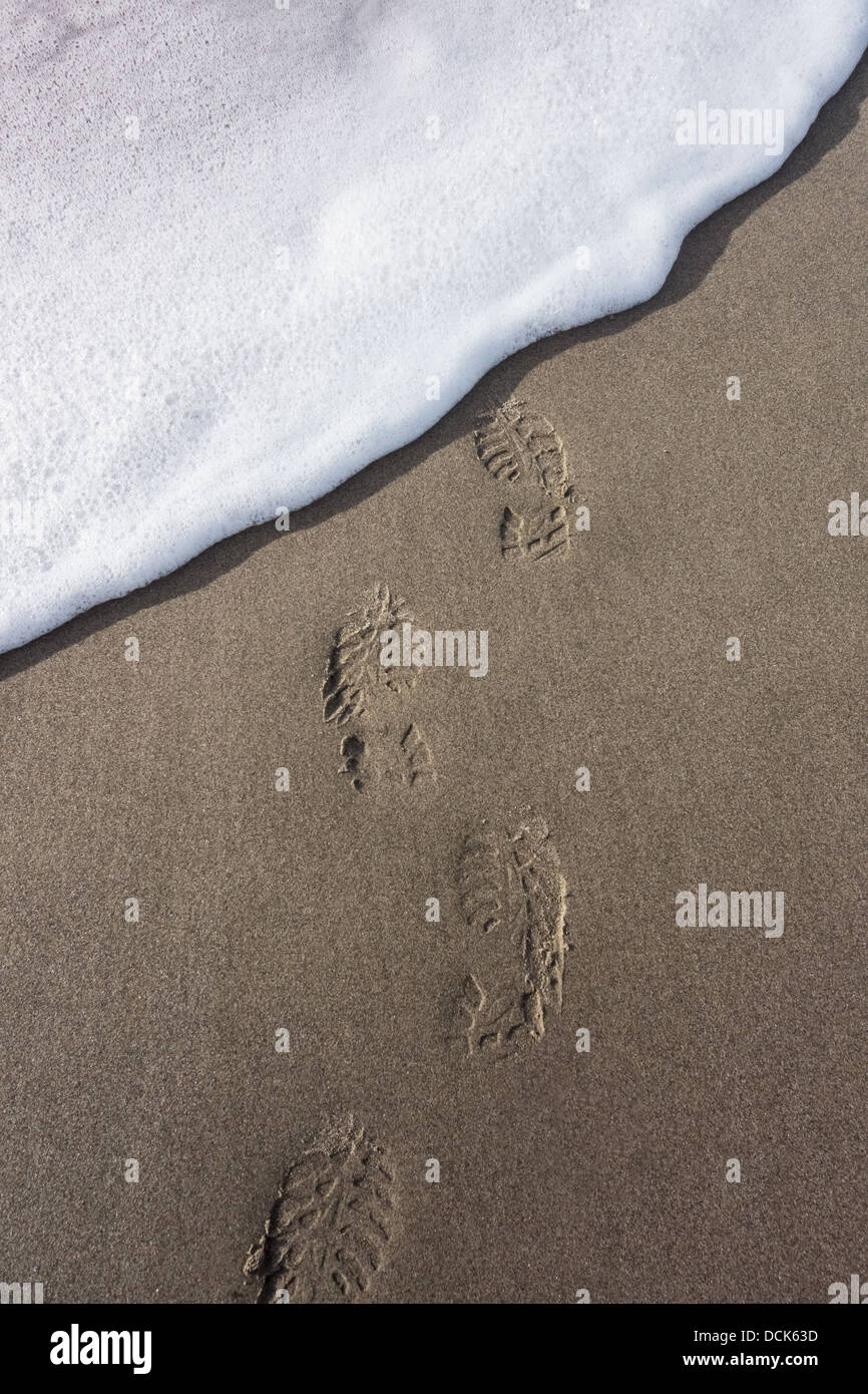 A line of boot prints in the sand are washed away by surf