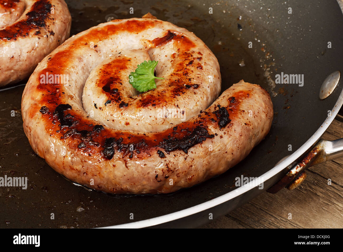 Coil of Traditional Cumberland Sausage being fried in a frying pan and starting to brown Stock Photo