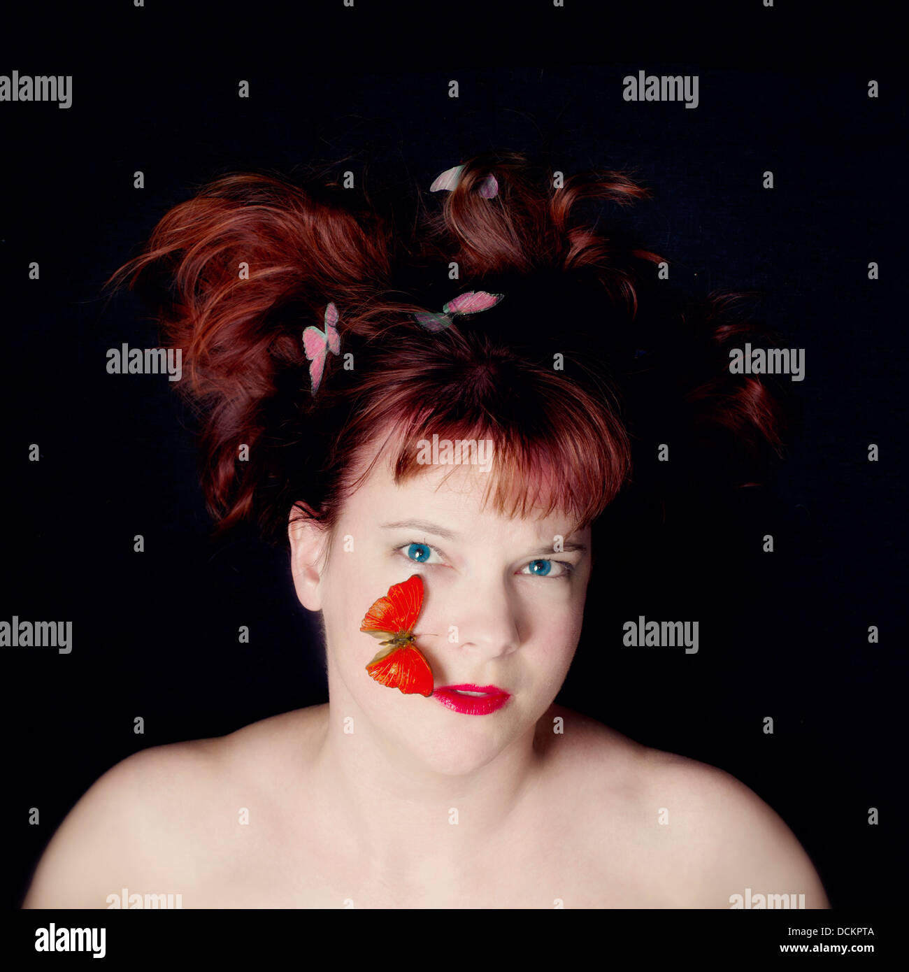 Face and shoulders of redhead with red lips and red butterfly on cheek. Stock Photo