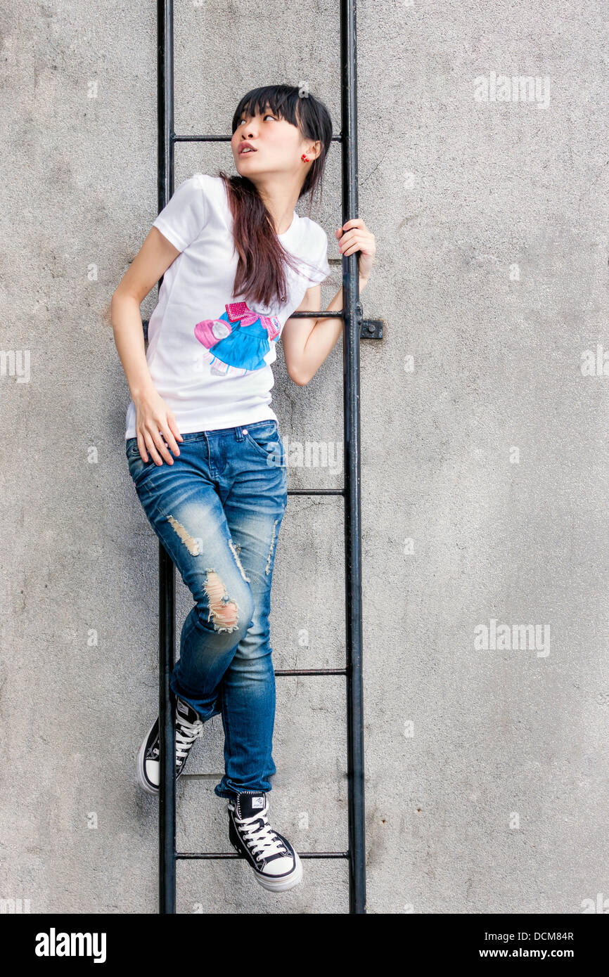 Asian girl on a ladder by limestone wall Stock Photo