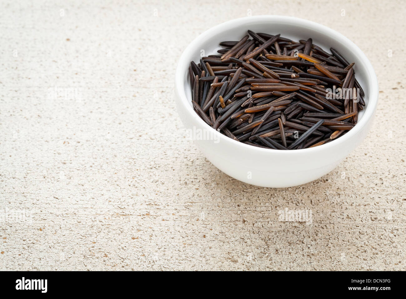 a small bowl of wild rice grain against rough white painted wood background with a copy space Stock Photo