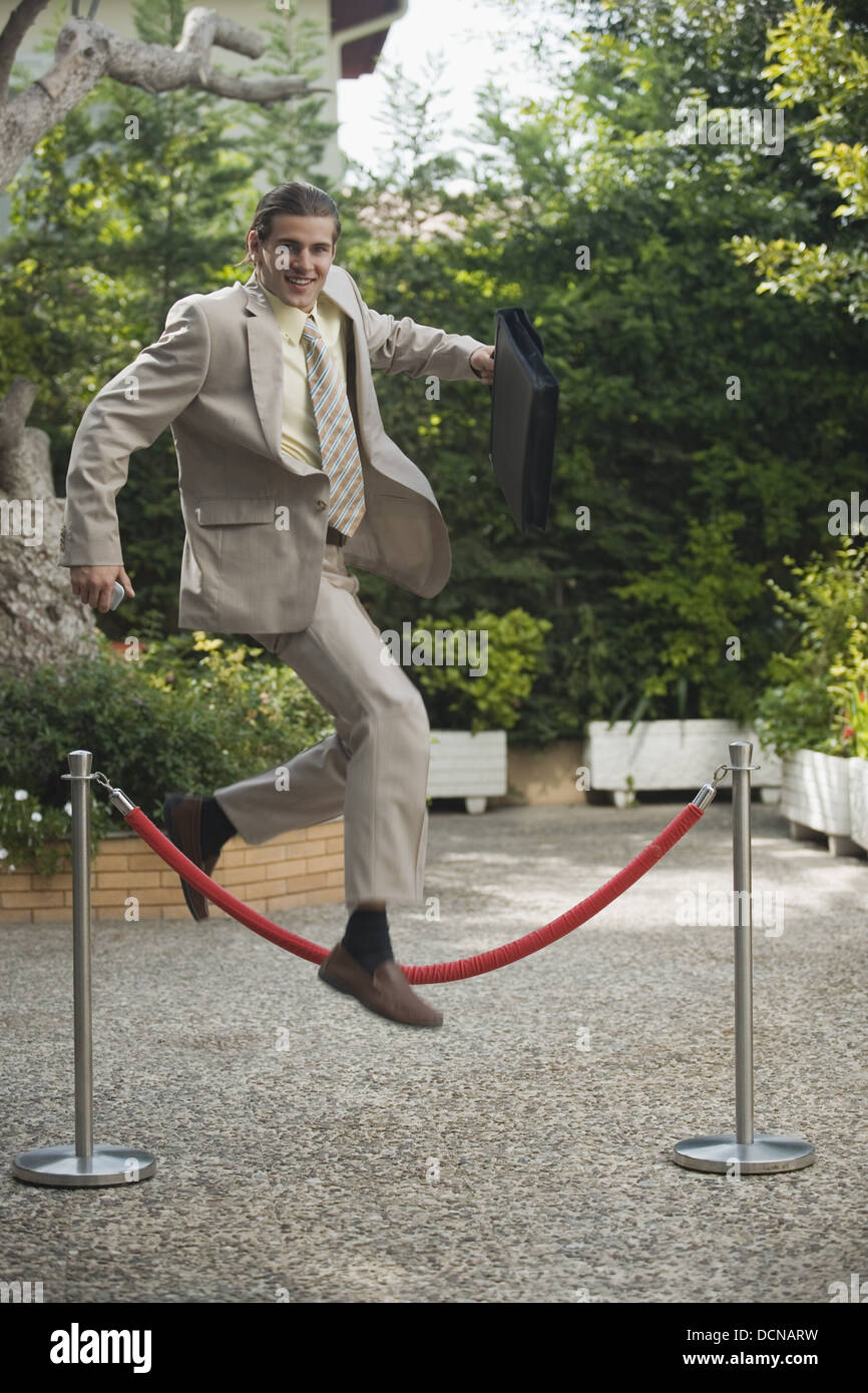 Businessman in garden jumping over barrier Stock Photo Alamy