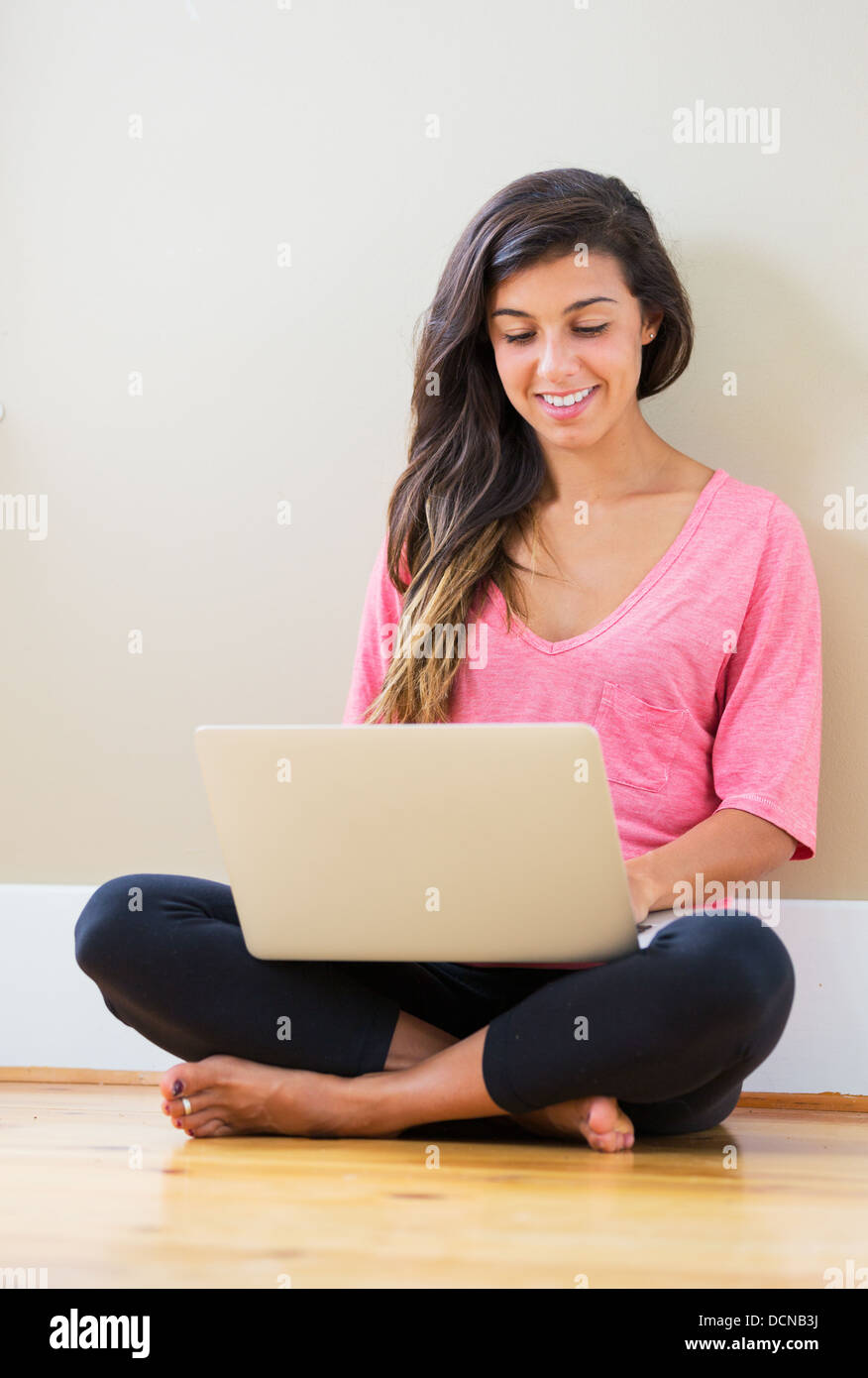 Portrait of beautiful happy young woman sitting on floor with a laptop ...