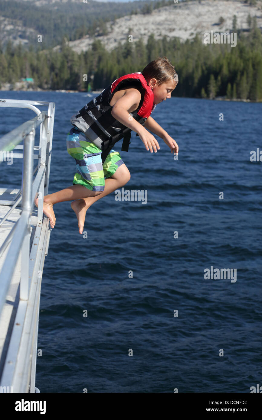 Young boy jumping off boat into lake Stock Photo