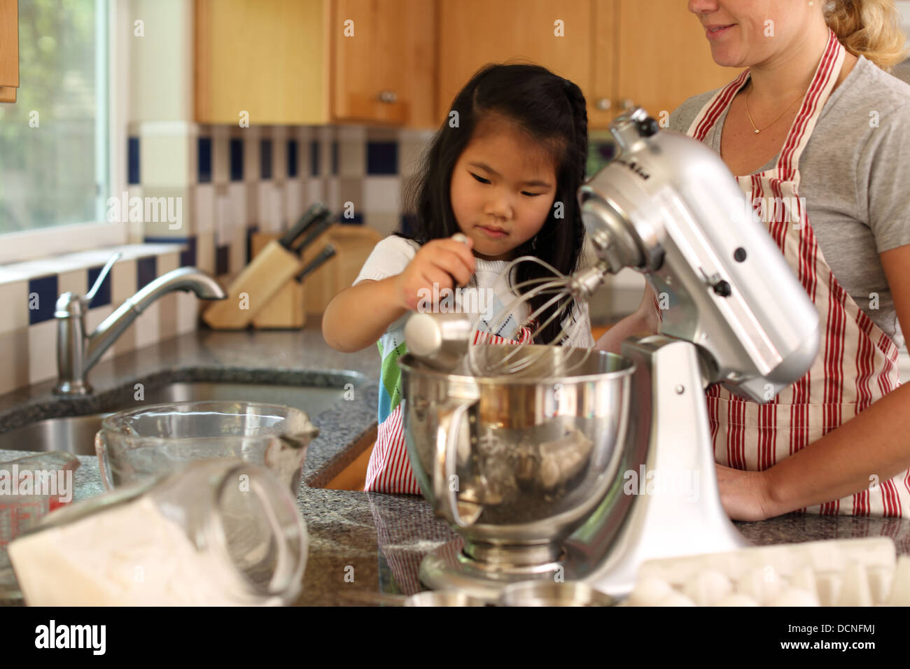 Young girl helping mother bake in kitchen Stock Photo