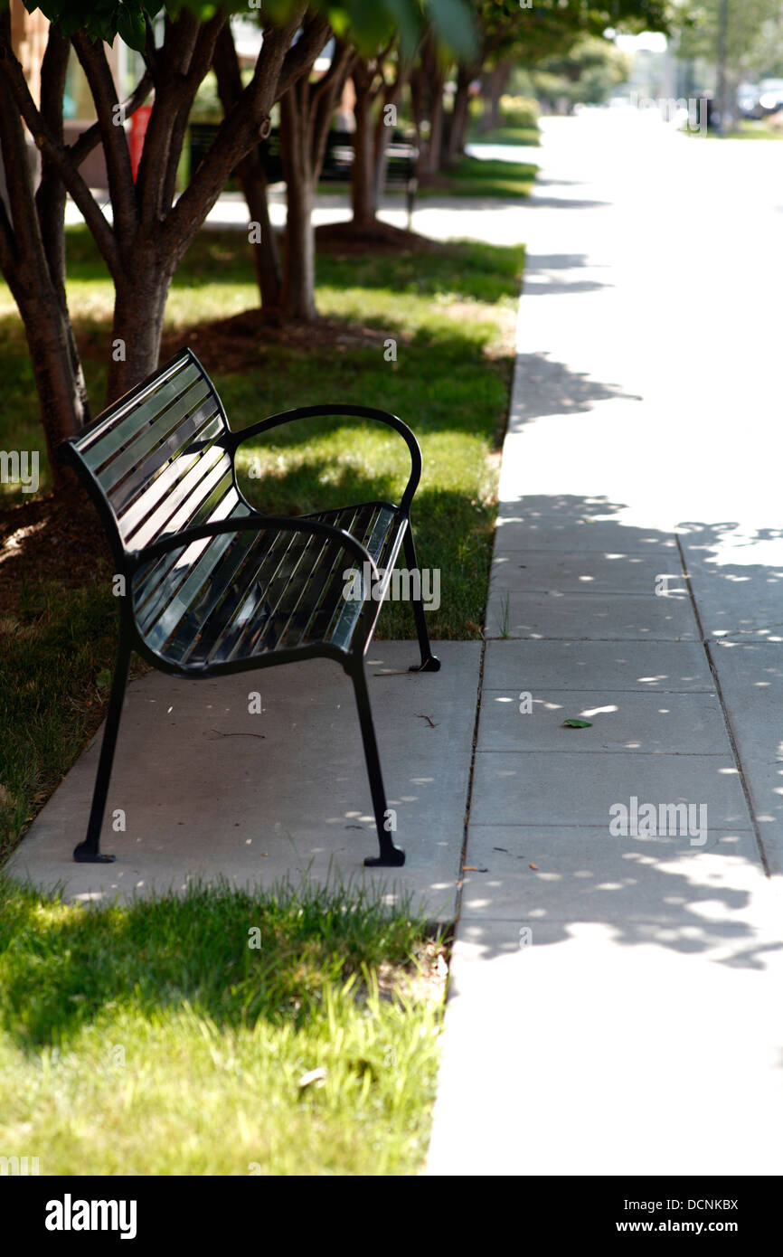 Shaded bench along sidewalk. Stock Photo