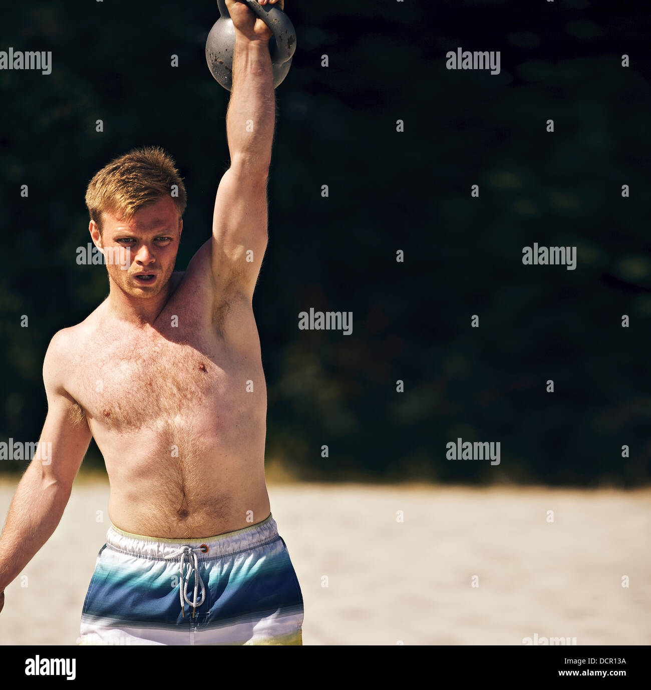 Guy lifting a heavy kettlebell on a beach during crossfit workout. Copy space right. Stock Photo
