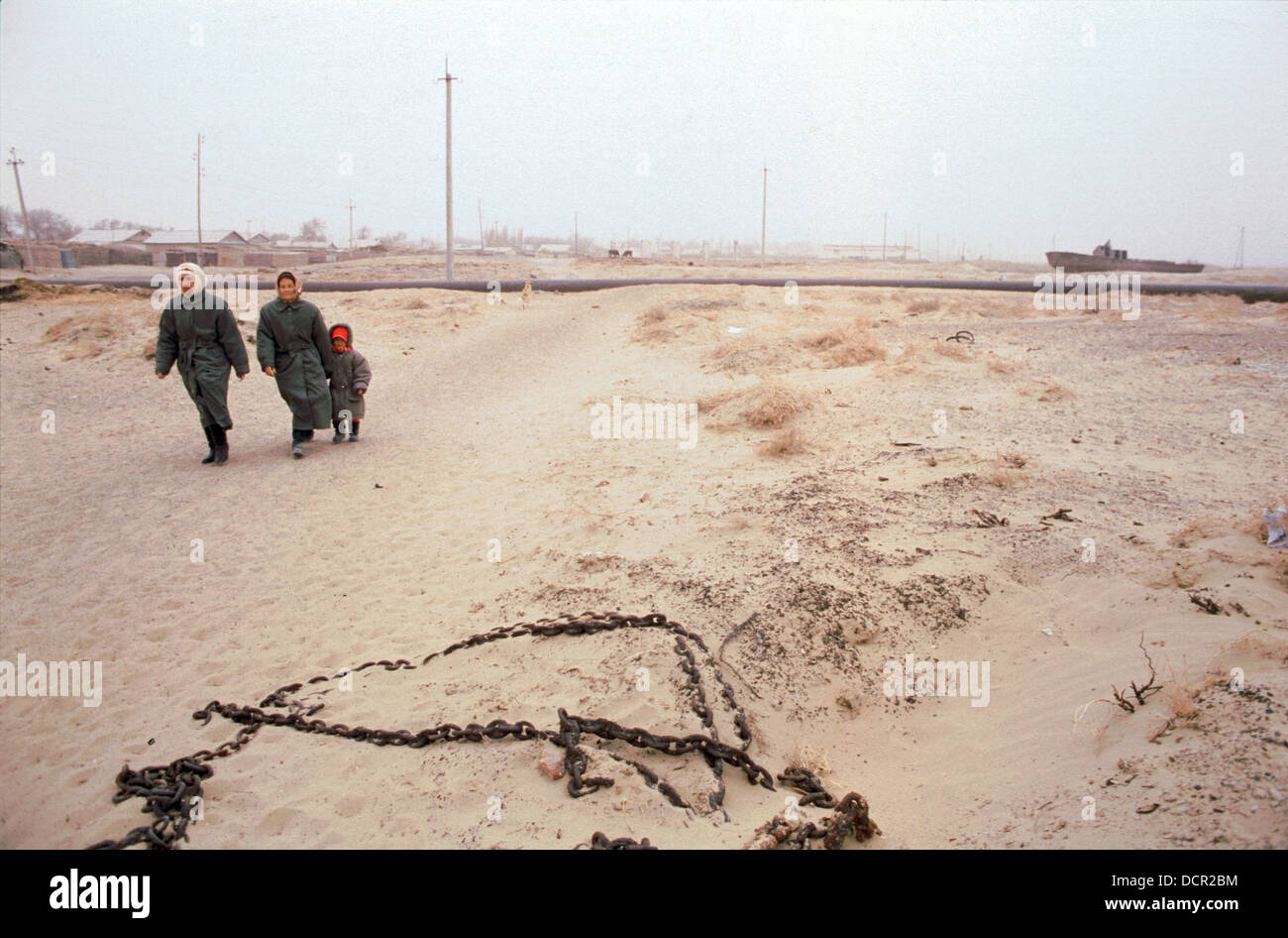 Residents walk through drifting toxic sand in the defunct port at Moynaq Uzbekistan. Once a thriving fishing port on the Aral Sea the coastline is now 60km from here due to shrinkage of the Aral. Many people here now have incurable respiratory illnesses Stock Photo