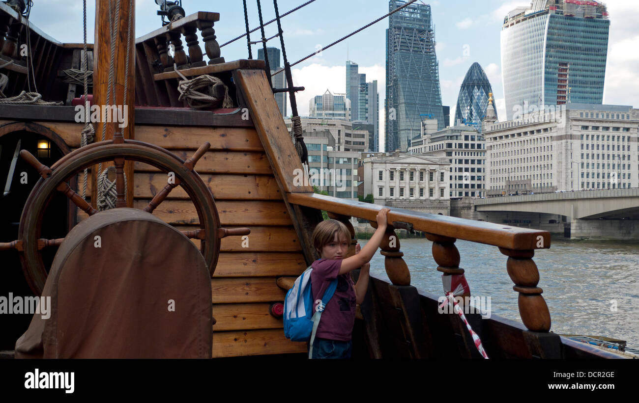 A boy on Sir Francis Drake's replica ship Golden Hinde and view of City of London  buildings across River Thames UK KATHY DEWITT Stock Photo