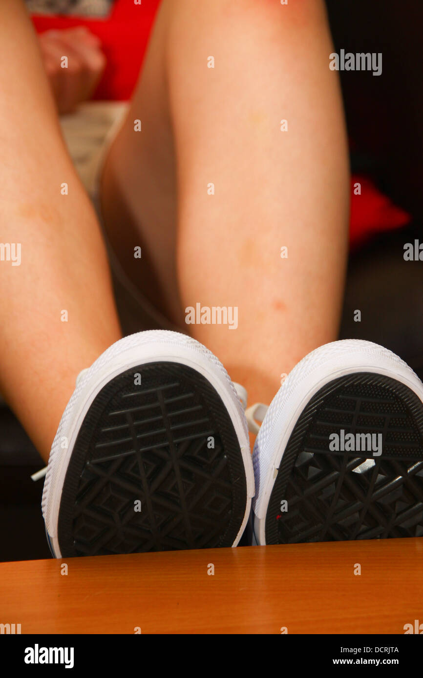 Girl wearing Converse shoes and resting feet on table Stock Photo